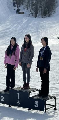 students stand on podium set out on snow with 1, 2 and 3 written on podium