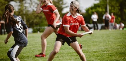 student in red uniform is about to throw a frisbee on a field