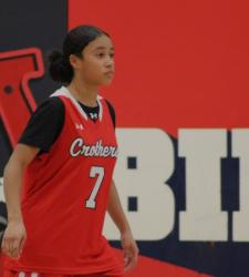 student playing basketball in front of school logo