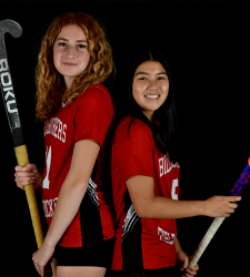 two students holding field hockey sticks